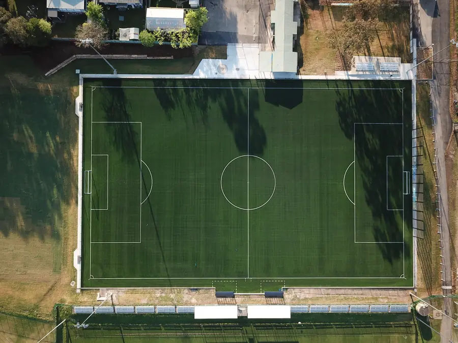 Top-down aerial of a full synthetic football pitch with grandstand seating at Popondetta Park