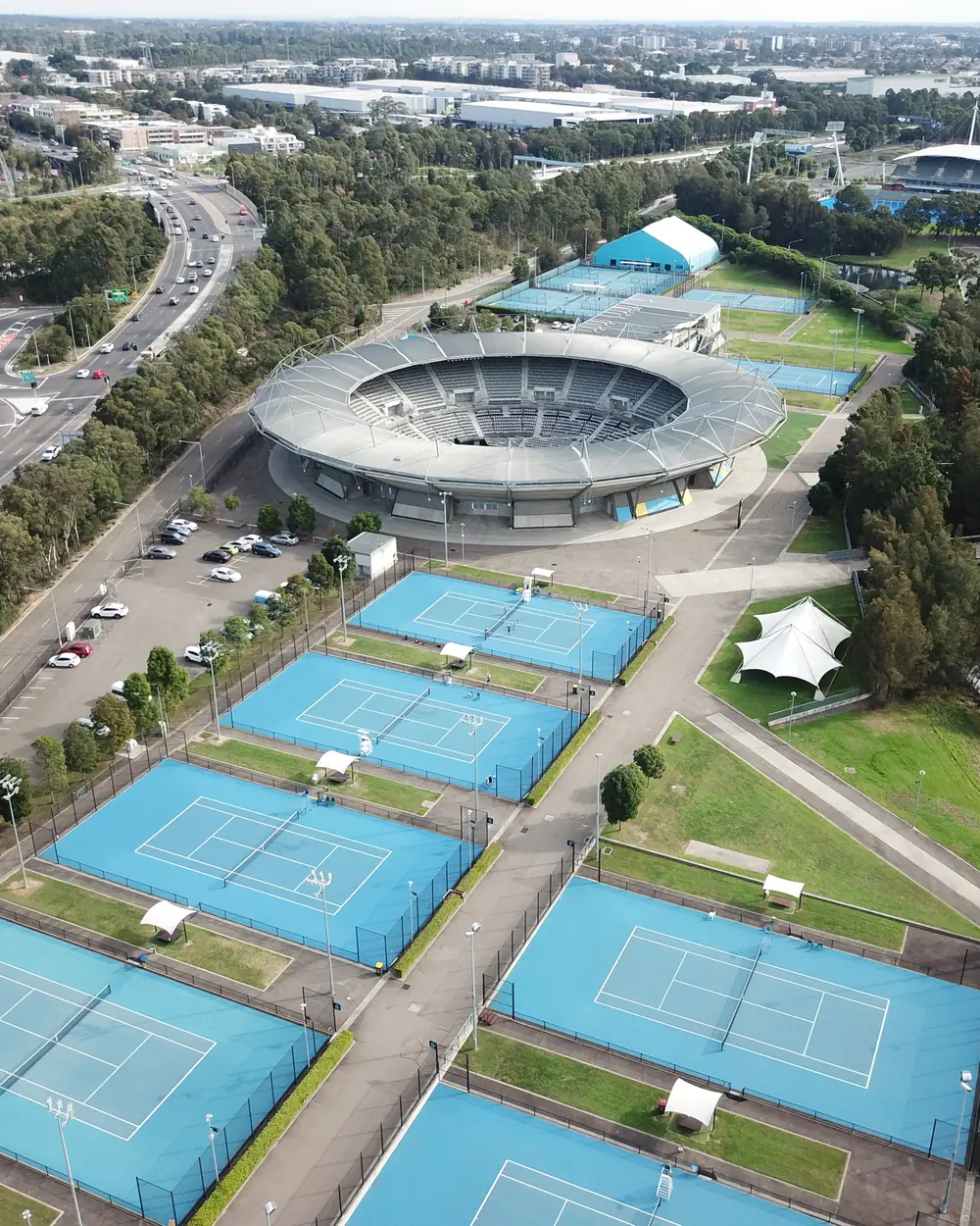 Aerial view of the Sydney Olympic Park tennis precinct, showing the show court arena and rows of blue outdoor courts